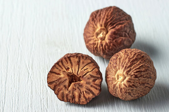 Whole and Halved Nutmeg Seeds on Light Wooden Background