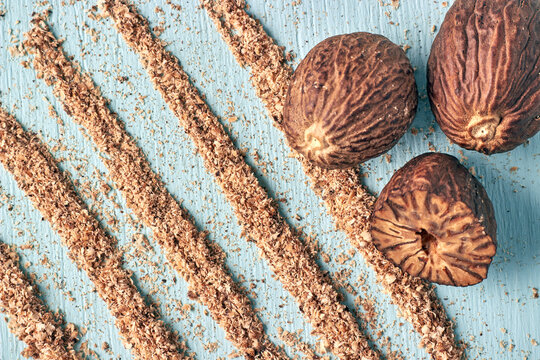 Grated and Whole Nutmeg Seeds on Blue Wooden Background