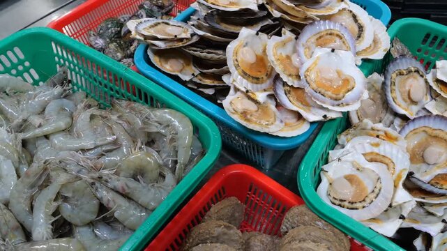 Fresh seafood items including raw shrimp, assorted scallops, and abalone are organized inside colored plastic baskets and carefully arranged onto metallic trays for culinary service
