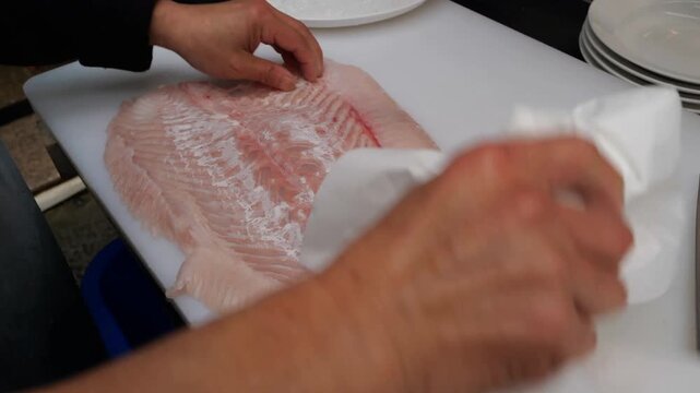 Commercial kitchen preparation workflow showcasing precision culinary techniques for slicing and plating fresh fish fillets on clean white surfaces for restaurant service distribution