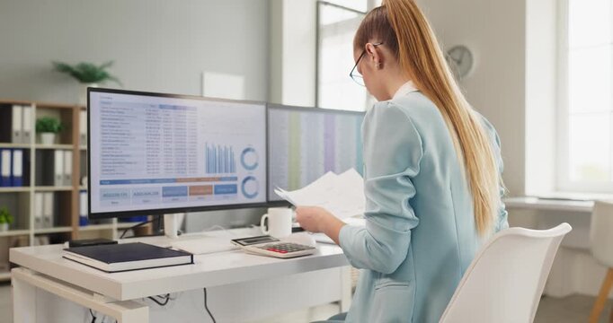 Accountant woman at computer in office workplace. Reviewing finance reports and doing accounting analysis on dual monitors for audit and QA. Clear professional financial oversight concept