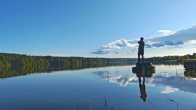 Silhouette of a man fishing while standing on a boat on a calm river at golden hour with sky reflections, peaceful angling scene, outdoor recreation, riverside serenity.