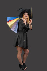 Woman dressed as a witch enjoying retail therapy with multiple shopping bags on her shoulder, happily holding a magic wand, celebrating sales and discount deals © somemeans