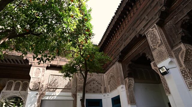 Marrakech, morocco. August 10, 2026. Traditional moroccan riad showcasing intricate islamic architecture. Sunlight filtering through an orange tree highlights the detailed carved wood and plaster