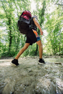 Hiker man with backpack crossing a shallow forest stream on a summer outdoor adventure