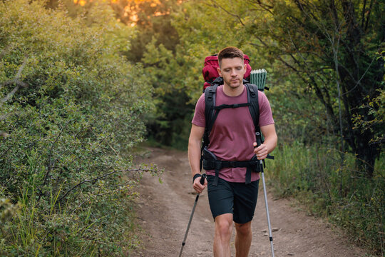 Handsome man trekking through woods path with backpack and poles