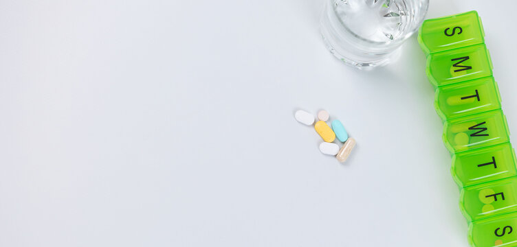 Weekly pill organizer with colorful medication and glass of water on white background. High quality photo
