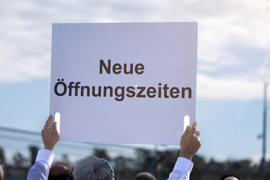 (Fotomontage) Ein Schild mit dem Text NEUE &Ouml;FFNUNGSZEITEN wird in die H&ouml;he gehalten