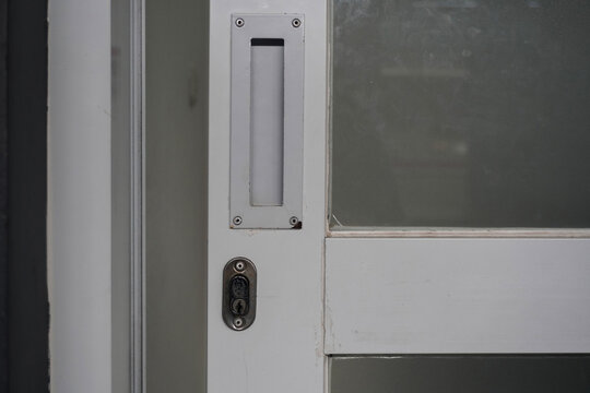 Close up of a white door with a mail slot and lock.