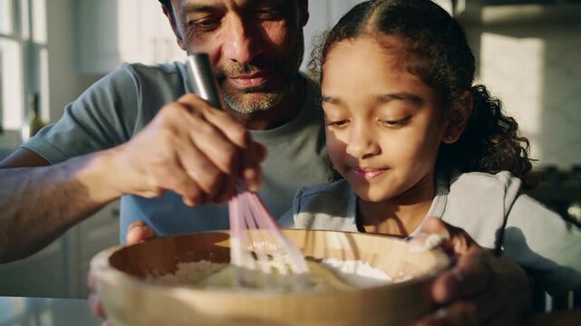 Starting whisking father in grey tee teaching daughter mixing at home with wooden bowl and whisk