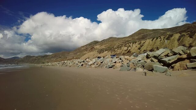 Beach area around the Ventura county line area of southern California. Deep blue skies, white clouds and mountainside. Stabilized handheld slow motion shot.