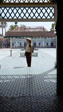 Marrakech, morocco. August 10, 2026. Caucasian woman with a hat and backpack standing in a traditional moroccan courtyard. Beautiful mosaic tiles and architecture in marrakech