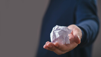 Crumpled paper in an outstretched hand symbolizes creative frustration, discarded ideas, problem solving, failure, brainstorming, rejection, the process of developing better solutions, new concepts. © Bordinthorn