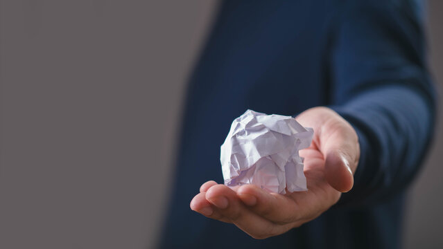 Crumpled paper in an outstretched hand symbolizes creative frustration, discarded ideas, problem solving, failure, brainstorming, rejection, the process of developing better solutions, new concepts.
