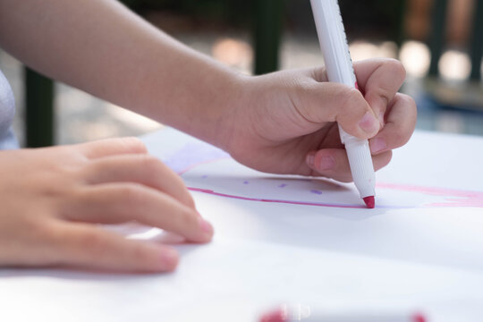 Child drawing with a colorful marker on paper during a creative activity, developing fine motor skills, concentration, imagination, hand coordination, self-expression, learning, childhood creativity.