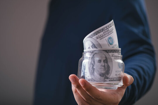 Person holding a glass jar filled with US dollar bills, symbolizing saving money, personal finance, wealth accumulation, financial security, budgeting, investment, income, and future planning.