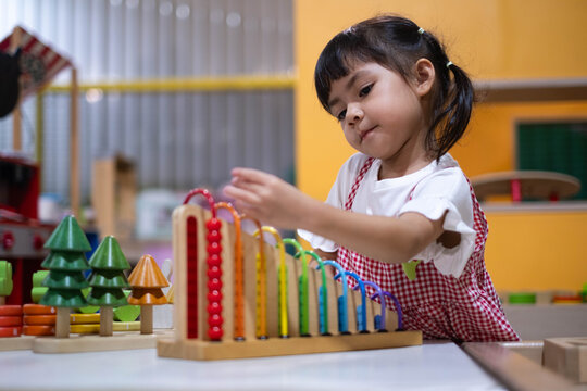 Young girl playing with a colorful wooden abacus toy in a preschool classroom, developing counting, concentration, coordination, problem solving, creativity, learning, and early childhood skills.