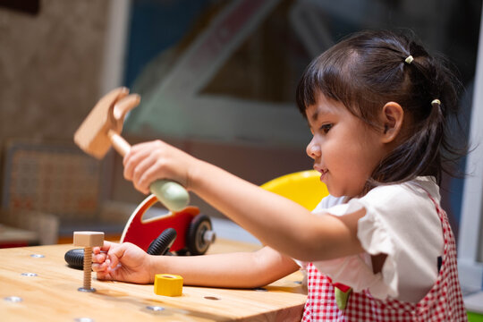 Young girl using a toy hammer at a pretend construction workshop, repairing a toy vehicle while exploring mechanic roleplay, creativity, problem solving, practical skills, imagination, and learning.
