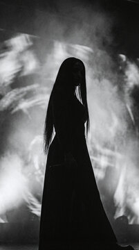 Silhouetted female figure with long dark hair standing against dramatic cloudy sky backdrop