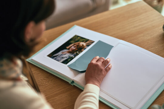 A woman casually gazes at a family photo in an album, conveying a reflection of memories while reminiscing her loved ones in a cozy and serene environment.