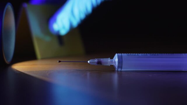 Blue gloved hand placing evidence marker near bloody syringe, revealing tense realization of crime under flashing police lights, rack focus extreme close up
