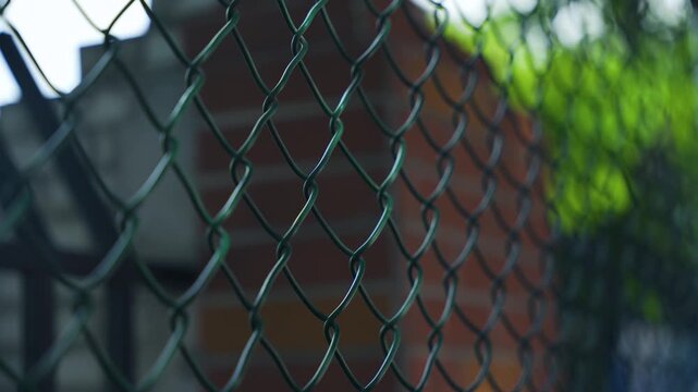 Close-Up of Green Chain-Link Fence with Blurred Brick and Foliage Background