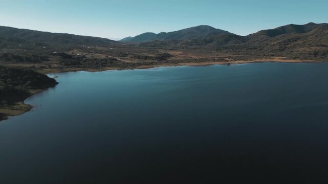 Aerial sweep over a calm reservoir tracing a rugged mountain shoreline