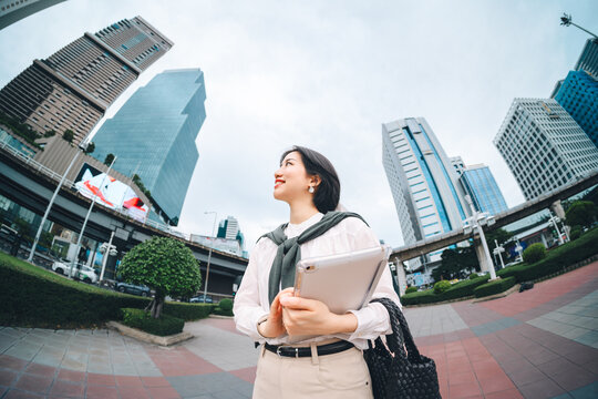 Positive smiling adult business asian woman walking to work in metropolis city shot in wide angle