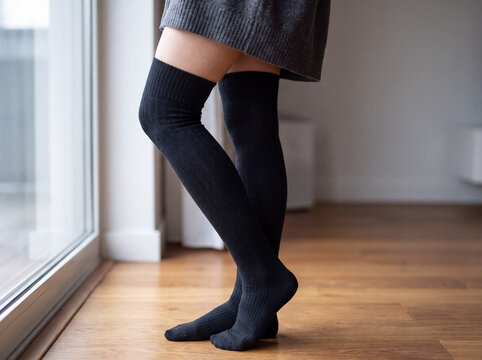 Woman's legs wearing long black socks, standing on a wooden floor near a window, showcasing comfortable fashion and warmth