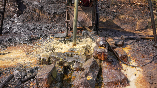 Long steel pipe extracting crude oil with dynamic water splash at historic Wonocolo traditional well, Bojonegoro, East Java, Indonesia. Authentic artisanal petroleum mining and energy production.