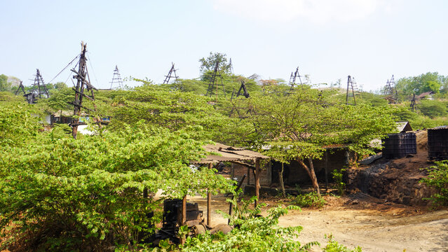 Traditional crude oil mining site with wooden derrick rigs and manual extraction equipment in Wonocolo village, Bojonegoro, East Java, Indonesia, surrounded by green forest landscape and hills.