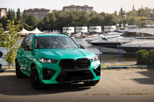Car Tiffany green BMW X5 parked near luxury yachts and forest background under a clear blue sky. Premium SUV lifestyle photography, vibrant summer atmosphere, modern automotive design