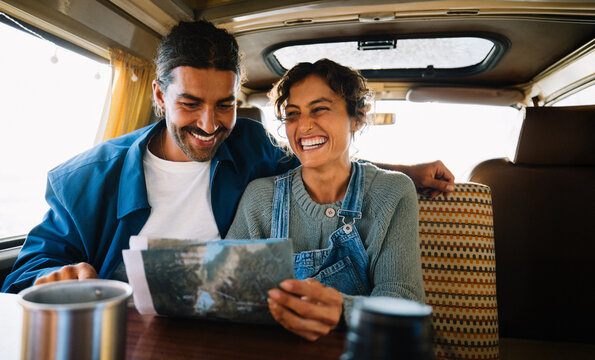 Traveling couple laughs over map in camper van on road trip