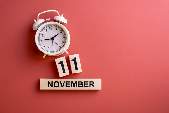 White alarm clock beside wooden number blocks showing November 11 on a clean coral pink background with generous copy space.