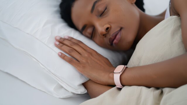 Sleeping woman wearing pink bbt tracker in bed, wearable basal temperature sensor for ovulation prediction, passive overnight fertility monitoring