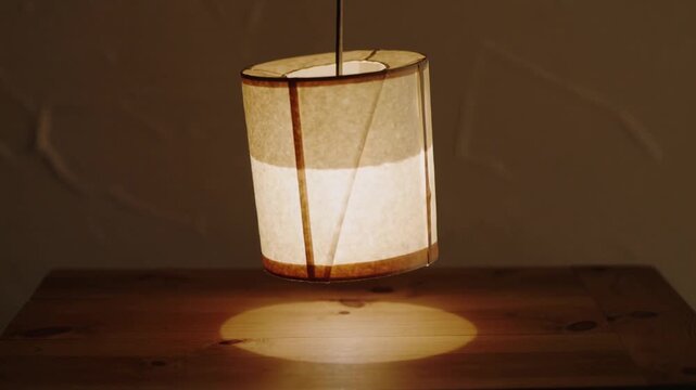 Swaying drum lampshade tilting after cord shift above wood table at home, casting round light pool