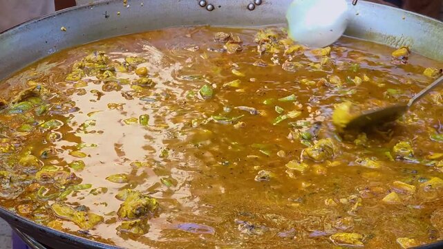 Close-up of chef stirring traditional Spanish paella with meat and vegetables simmering in rich golden broth during a cooking competition in Denia, Spain. Ideal for culinary, travel, and food concept