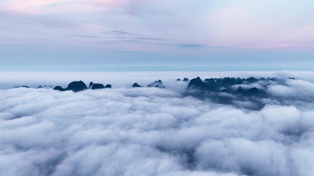 High angle view of karst mountain peaks emerging above a dense sea of clouds under soft morning twilight light in Guilin, China.