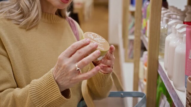 Mature unrecognizable woman examining skincare cosmetic jar in retail beauty store. Footage suits cosmetics advertising, organic skincare campaigns, consumer behavior projects