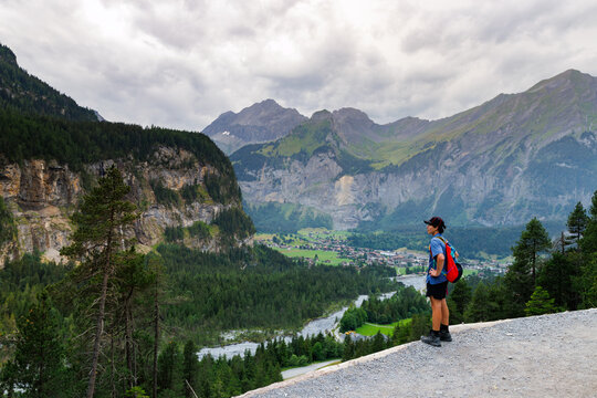 A young man with a backpack overlooking the town of Kandersteg Switzerland from a trail high above