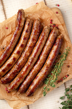 Juicy roasted grilled meat sausages served on parchment paper on wooden cutting board with herbs and spices