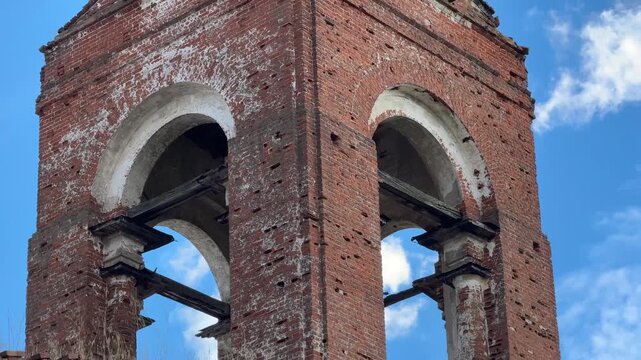 The ruined brick tower of the church with arched openings under a clear sky.