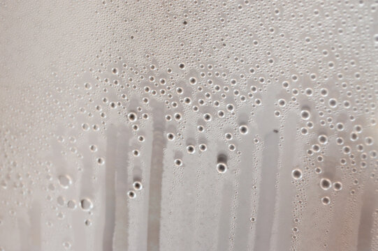 Water droplets leaking down a foggy transparent glass surface
