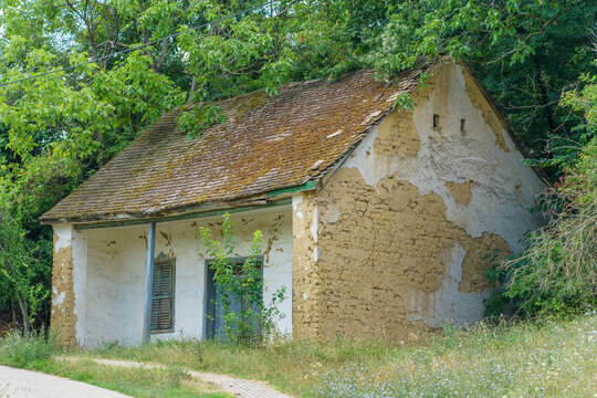 Old abandoned rural mudbrick house with peeling plaster and tile roof surrounded by green vegetation, traditional vernacular architecture and historic cottage