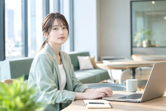 ビジネス オフィスでノートパソコン作業を中断して視線を向けるビジネスウーマン 自然光と広いコピースペースを生かした仕事風景