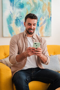 A focused adult interacts with a smartphone while relaxing on a bright yellow sofa in a tidy living room, conveying simple efficiency and everyday digital connection in a comfortable space for media!