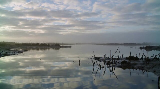 Rippling tidal channel from breeze, showing cloud reflections at marsh with mudflat and marsh grass
