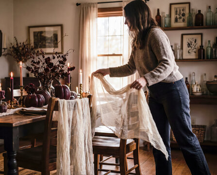 Woman draping sheer gauze fabric over dining chair for spooky halloween tablescape setup