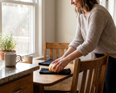 Smiling woman placing small white pumpkin on napkin at rustic halloween breakfast table