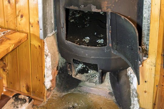 Open wood burning stove in rustic wooden sauna during seasonal maintenance